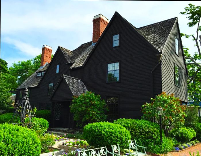 A striking black wooden house featuring several unique peaks and a well-kept garden