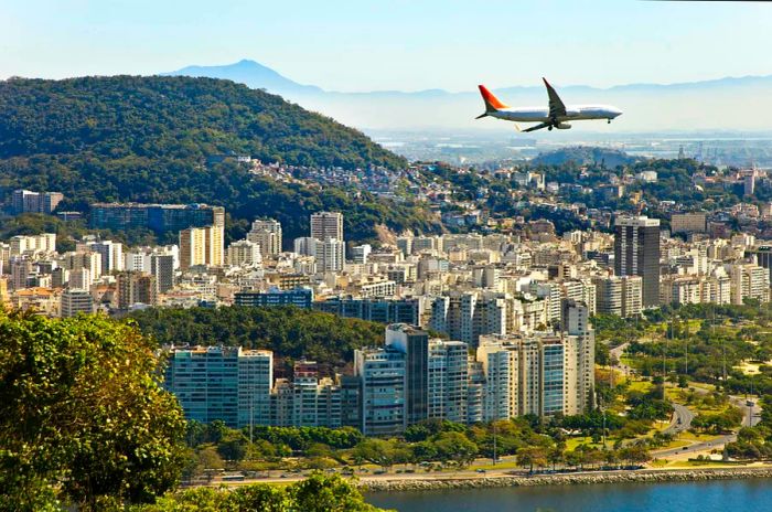 A commercial airplane soars over a densely populated coastal city