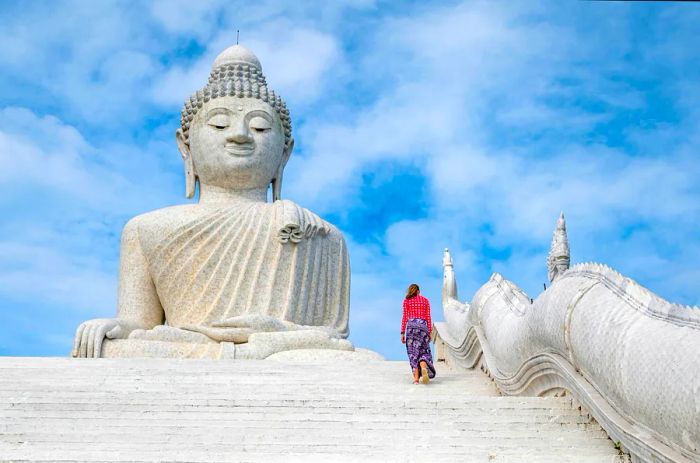 A teenager ascends steps towards an immense white marble Buddha statue