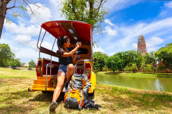 A backpacker captures photos of an ancient temple while riding in the back of a tuk-tuk (a small motorized vehicle).