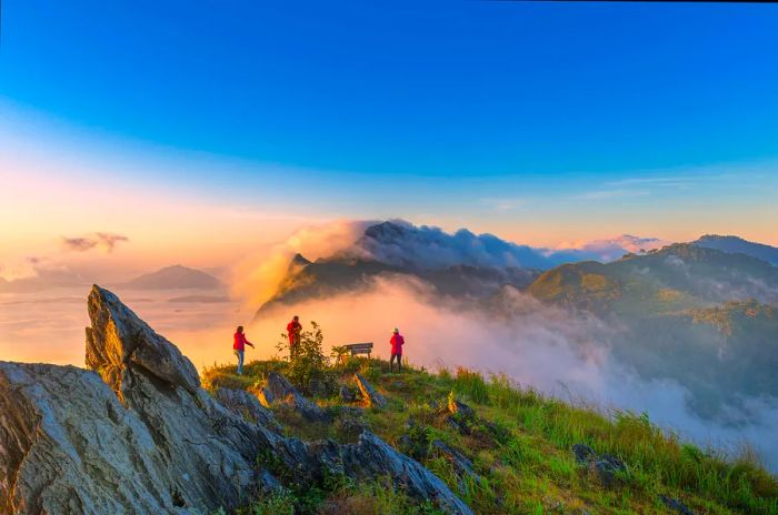 Three individuals enjoy a viewpoint atop a mountain, surrounded by clouds shrouding the landscape.