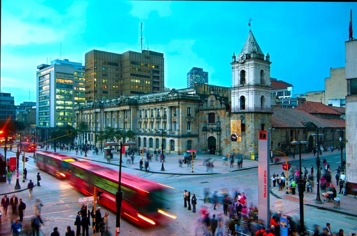 A red TransMilenio bus halts near the Iglesia de San Francisco, Bogotá, Colombia