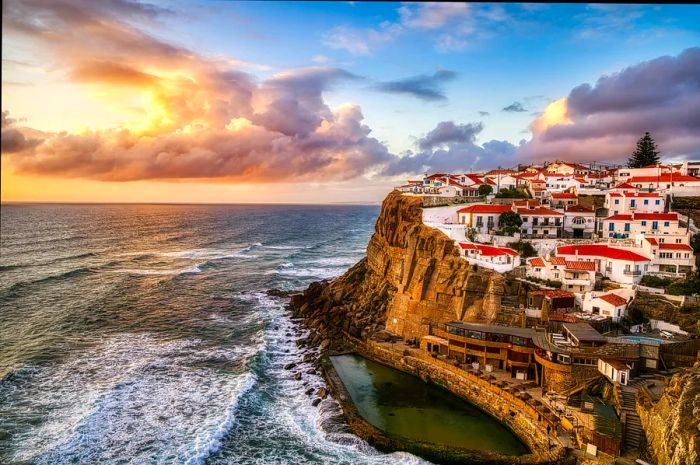 A breathtaking cliffside view of white houses lining a rugged coastline in Sintra at sunset