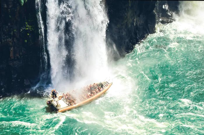 A speedboat filled with tourists glides beneath one of the many cascades at Iguaçu Falls