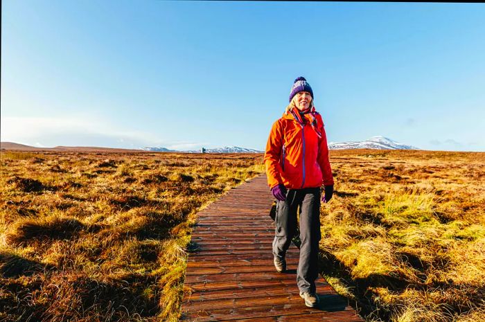 An elderly woman walks along the wooden path over the peat bogs at Forsinard, Sutherland, Scotland