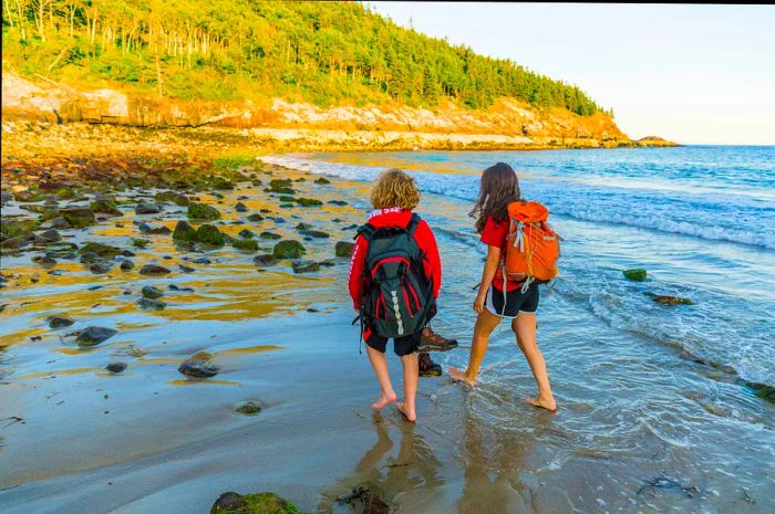 A teenage boy and girl stroll along Sand Beach after hiking in Acadia National Park, Maine.