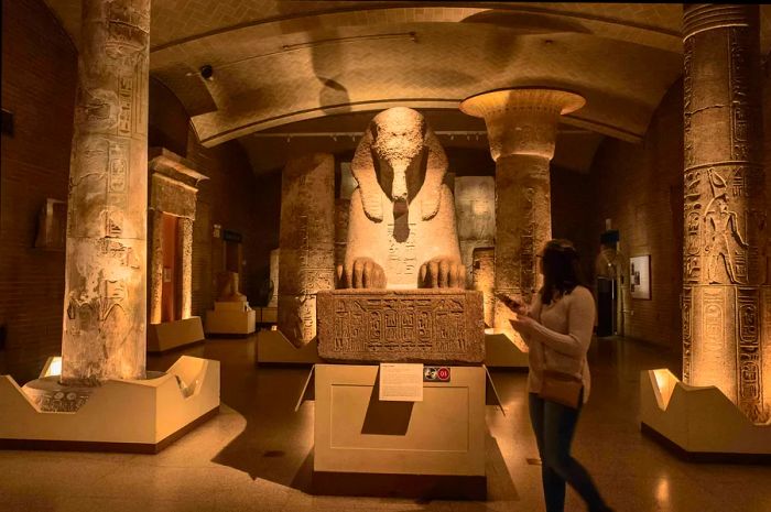 A visitor strolls past the Sphinx of Ramses II displayed in a dimly lit room at the Penn Museum in Philadelphia.