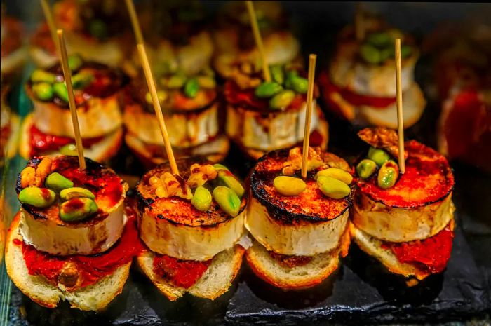 Traditional Spanish pintxos featuring goat cheese, pistachios, walnuts, and red piquillo pepper at a bar in San Sebastián (Donostia), Basque Country, Spain