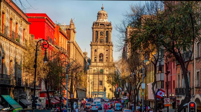 A bustling street filled with vehicles and pedestrians leads to the Zócalo and the Metropolitan Cathedral in Mexico City, Mexico.