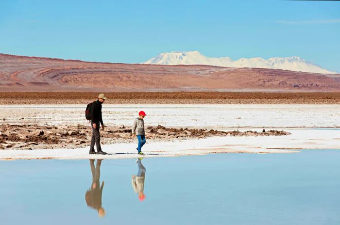 A father and son stroll beside a salt lake in an expansive desert landscape