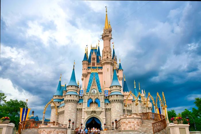 Visitors gather at the grand entrance of a whimsical pale pink castle with many turrets