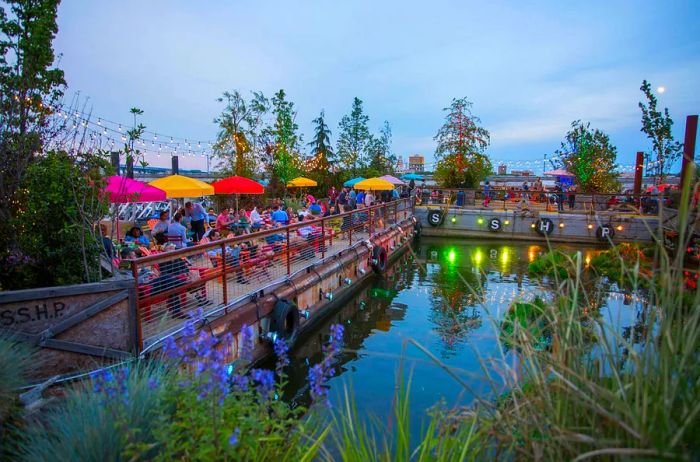 Wide view of a park set up along the river with red and yellow umbrellas shading tables