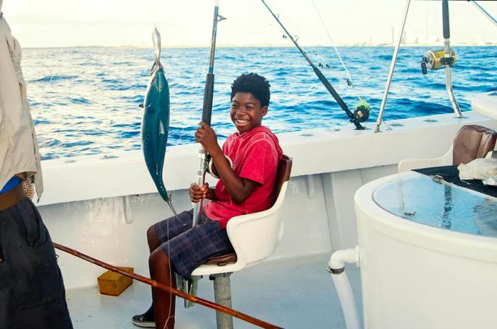 A preteen boy beams as he catches a fish while deep-sea fishing on a boat.