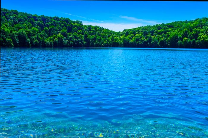 On a sunny day, enjoy the vibrant blue waters lapping against a rocky shore, framed by trees at Green Lakes State Park, New York.