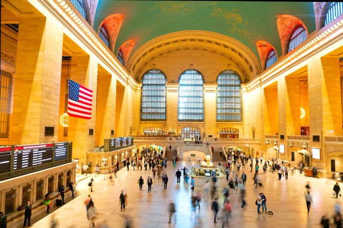 A blurred scene of visitors at Grand Central Station featuring a prominent American flag.