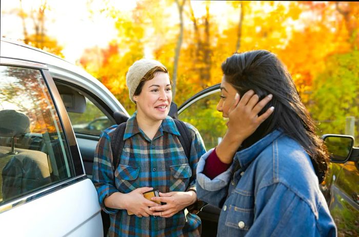 Two female friends of diverse ethnic backgrounds meet by the car in upstate New York during autumn.