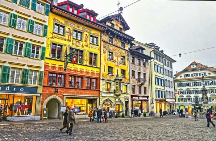 A city square is lined with medieval buildings embellished with murals.