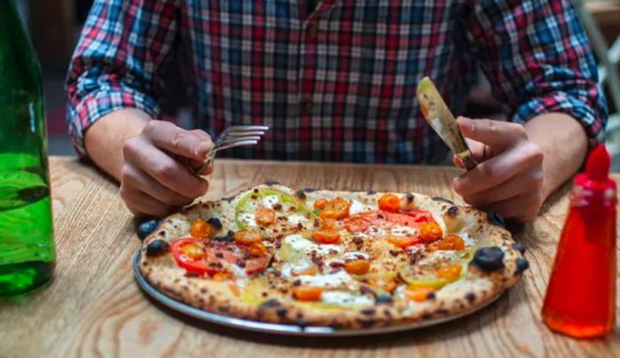 A person enjoying a pizza using a knife and fork