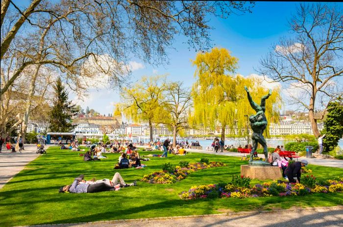 People lounge on the grass in a lakeside park on a sunny day