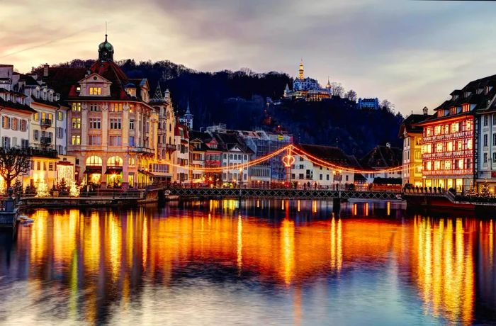 A city intertwined with a river, illuminated beautifully at night, with a castle peeking through the forest atop a hill.