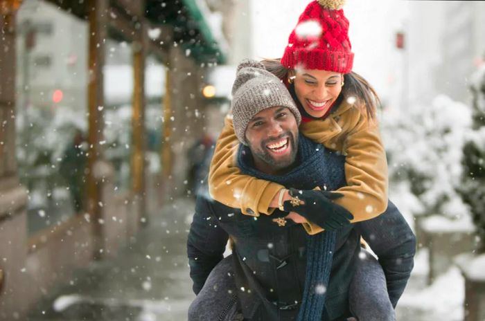 A joyful man carries a happy woman on his back in New York City as snowflakes fall around them.