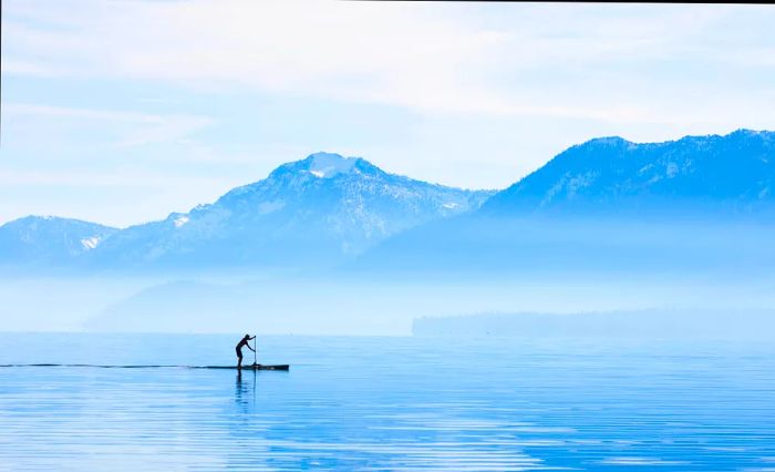 A paddleboarder enjoys a morning cruise along the shores of Tahoe City. Lake Tahoe, nestled in the Sierra Nevada Mountains, is a stunning high alpine lake in California.