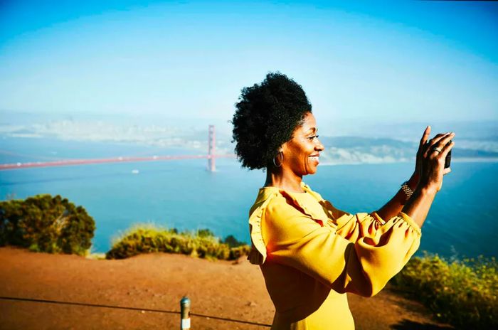 A joyful woman captures the moment with her smartphone while enjoying the view of the Golden Gate Bridge in San Francisco, California