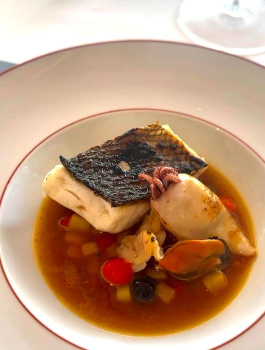 A white bowl filled with a trout and octopus soup