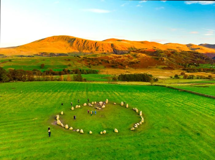 Visitors walking among a circle of ancient standing stones in a picturesque, hilly landscape