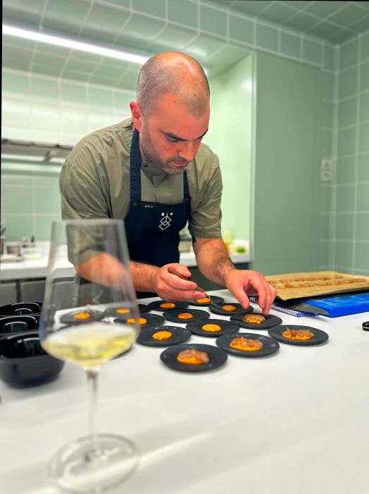 A chef meticulously prepares delicate dishes on small round black plates in an upscale dining setting