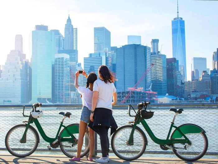 A couple with bicycles takes a moment to snap a photo of the NYC skyline.