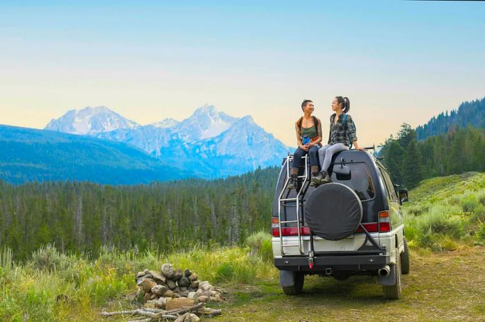 Two women relax atop a four-wheel drive vehicle in a mountainous area.