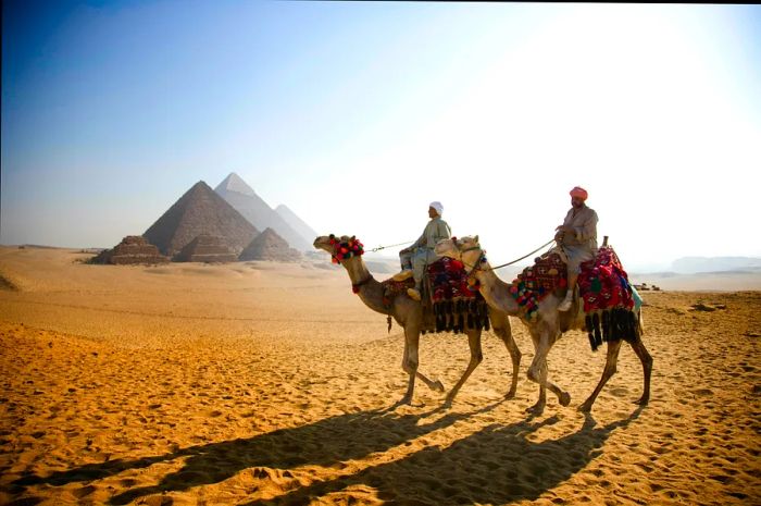 Two men on camels in front of the Pyramids of Giza, Egypt