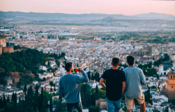 Three individuals stand at a high vantage point, gazing out over a city towards the mountains