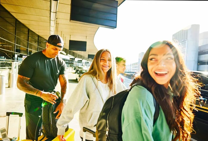 A cheerful group of travelers stands with their luggage at the airport curb.