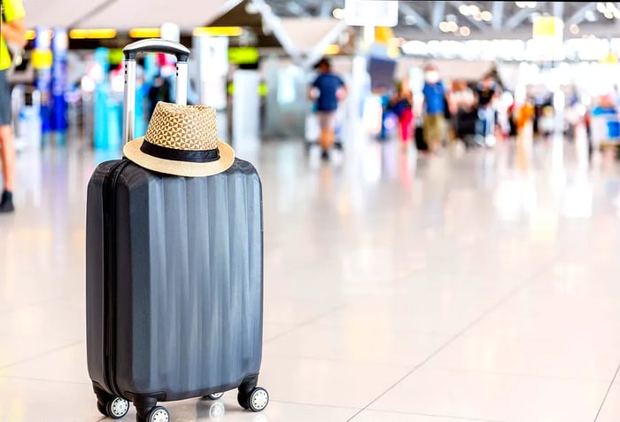 A straw hat perched on a suitcase resting on the airport floor.