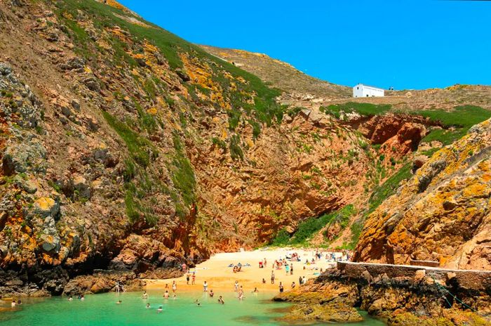 Visitors enjoy the beach and swim in the clear turquoise waters of a secluded cove framed by towering rocks.