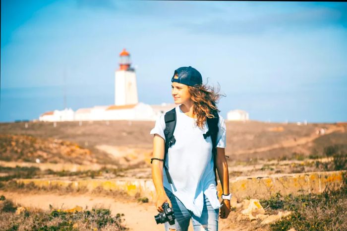 A photographer strolls along a path in a nature reserve, with a lighthouse visible in the distance.