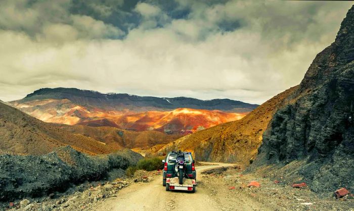 The rear of a four-wheel-drive vehicle towing a trailer with a dirt bike on a mountain trail