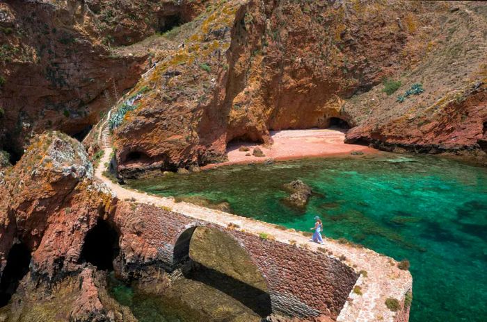 A person walks across a narrow stone bridge toward an island.