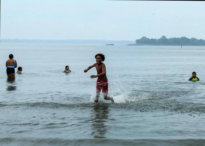 Children splash around in the shallow waters of Orchard Beach on a cloudy day in the Bronx, NYC.