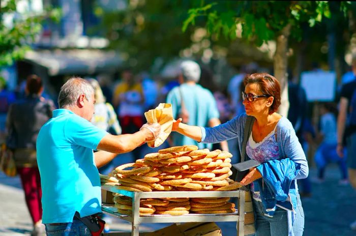 A woman purchases bread rings from a street vendor in Athens