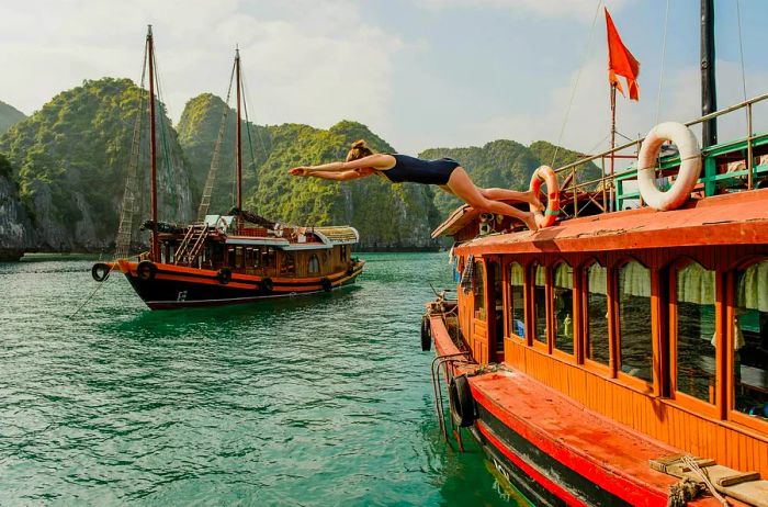 A woman leaps off a boat into a bay surrounded by towering limestone formations