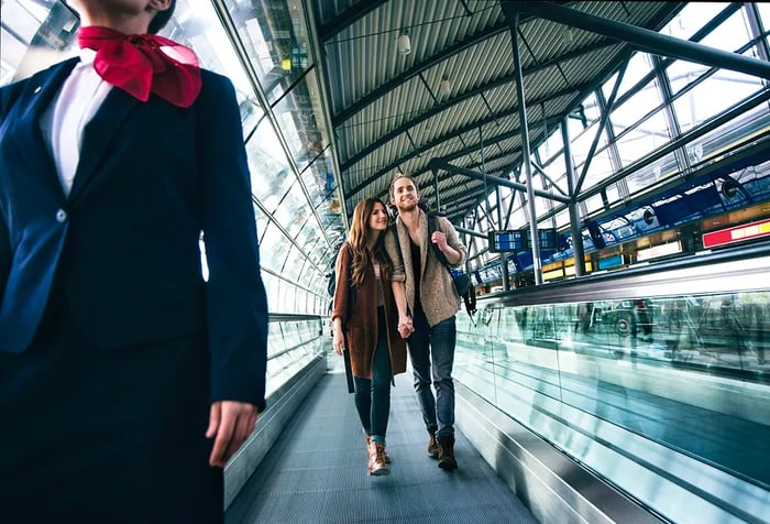 A young couple strolling along an inclined moving walkway in the airport.