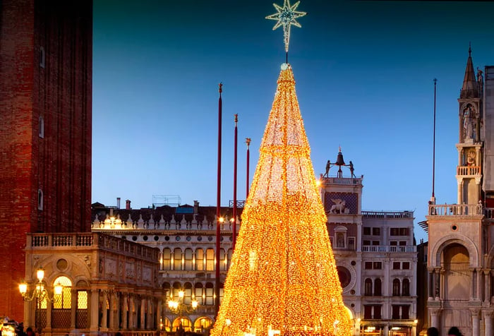 Renaissance-style buildings frame a grand Christmas tree adorned with yellow string lights.