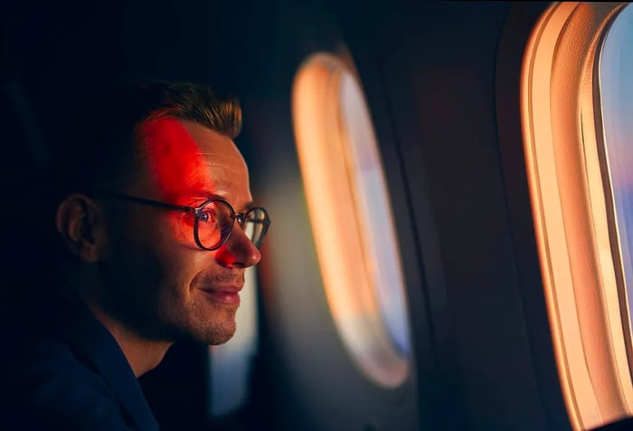 A man in glasses smiling as he gazes out the window of an airplane.