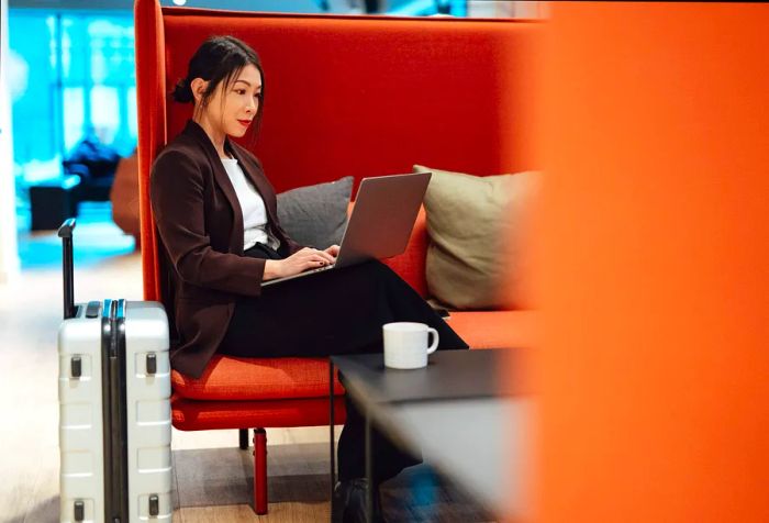 A businesswoman checks her emails on her smartphone while seated in an airport lounge, preparing for her departure. A young woman traveling for work.