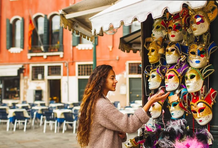 A woman with long, curly hair admires a mask showcased outside a souvenir store.