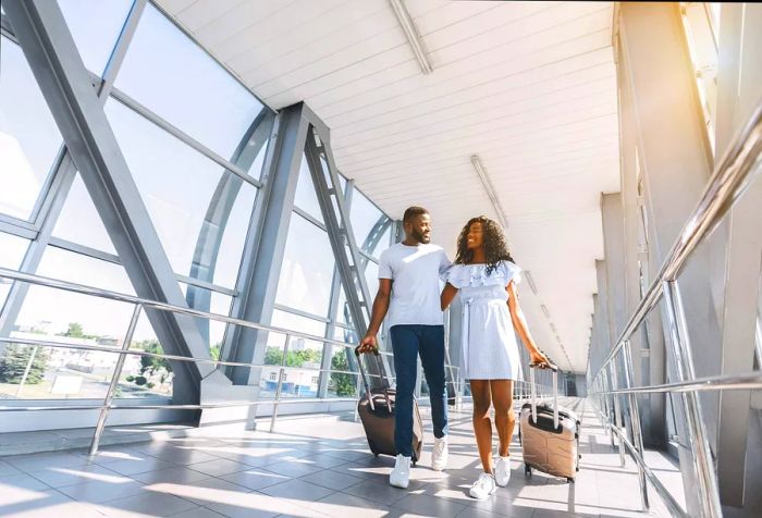 A couple strolling through the airport while handling their luggage.