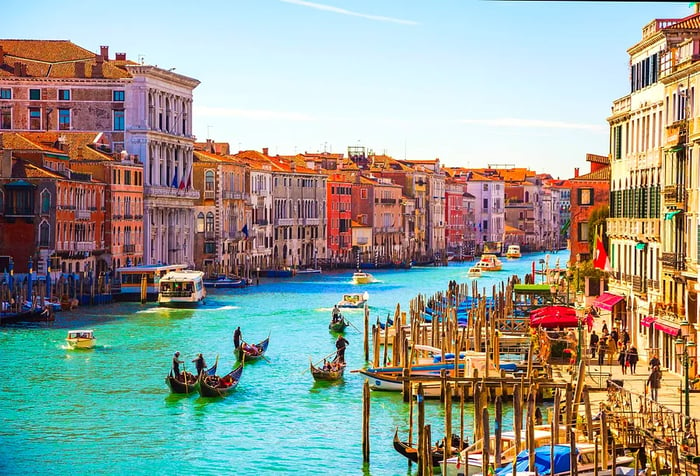 A canal flanked by charming buildings featuring anchored boats, along with gondolas and ferries gliding by.